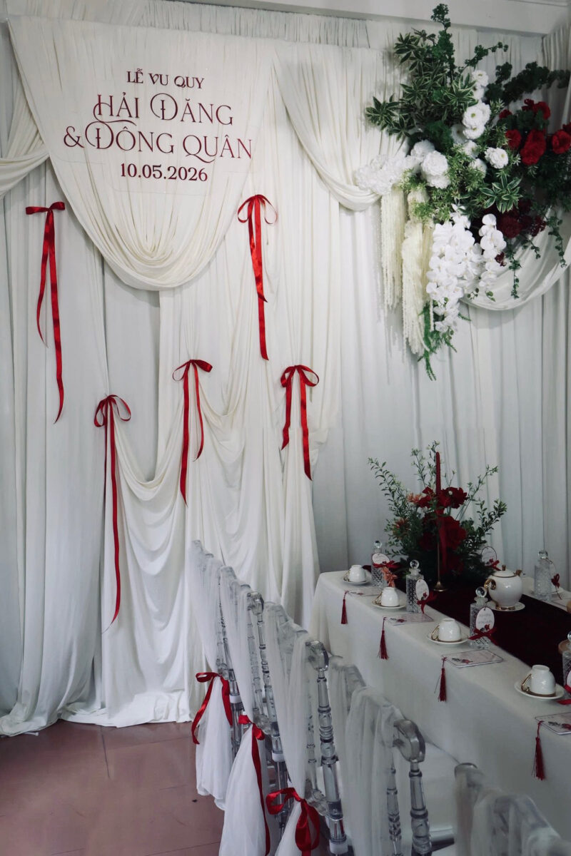 Mẫu trang trí gia tiên tone trắng đỏ hiện đại với bàn dài phủ khăn nhung đỏ và hoa decor sang trọng.