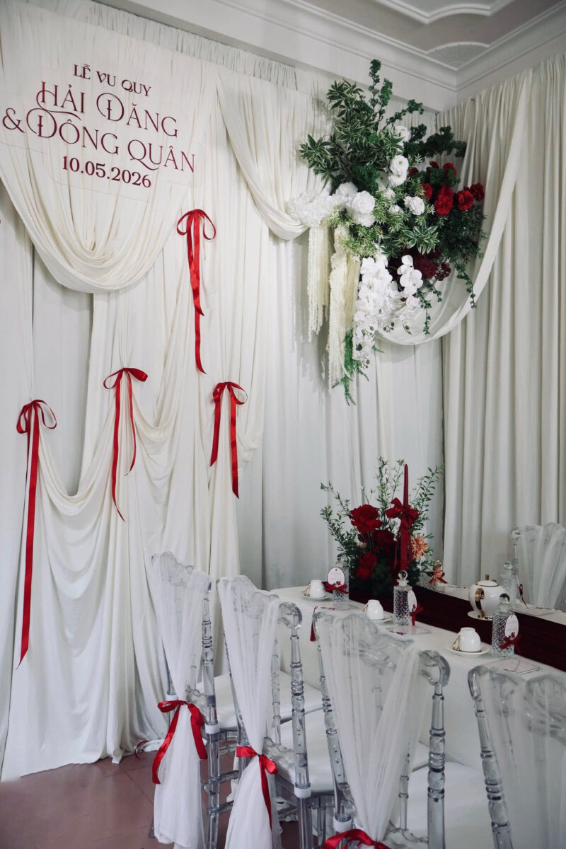 Backdrop gia tiên cưới hỏi tone trắng sang trọng cùng bàn tiệc phủ đỏ và ghế trong suốt cao cấp.